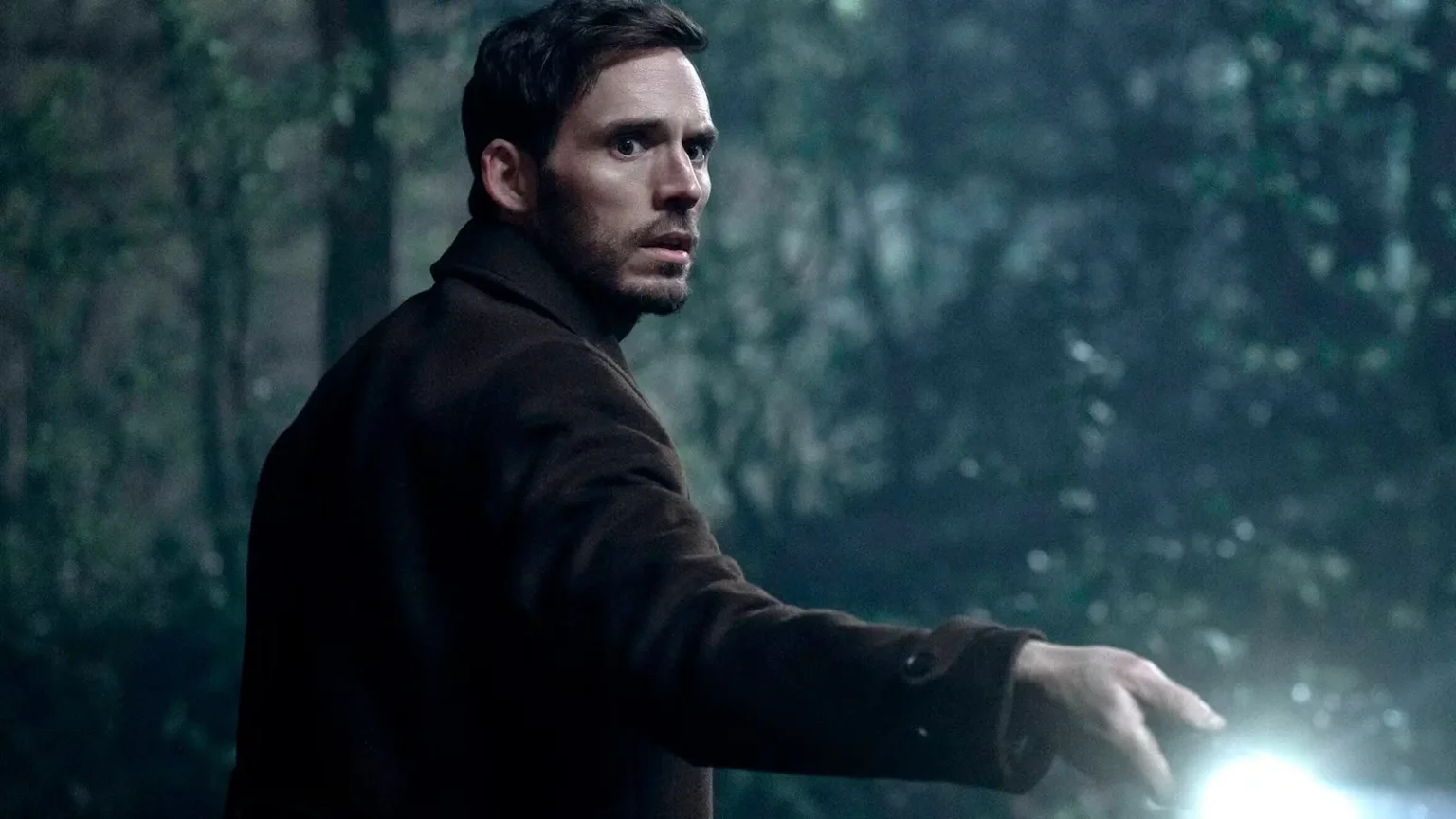 Harlan Coben: Lázaro é o novo suspense do Prime Video que vai mexer com sua mente Sam Claflin segura uma lanterna em floresta escura em cena tensa da série Harlan Coben: Lázaro do Prime Video
