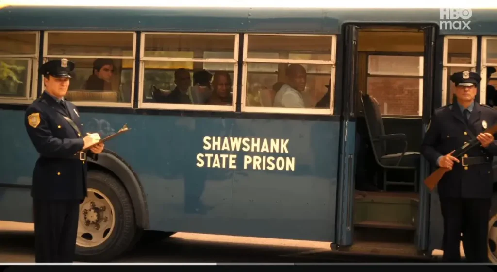 Ônibus azul com o nome “Shawshank State Prison” estacionado, com guardas e prisioneiros à vista, em IT: Bem-Vindos a Derry.