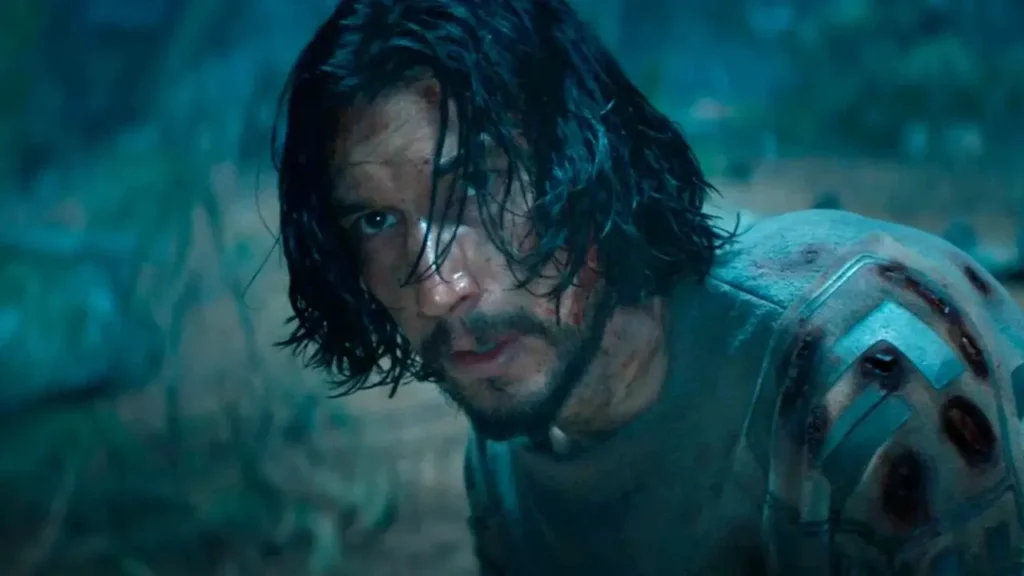 Adam Driver como Mills, ferido e coberto de sujeira, olhando em direção à câmera em ambiente de floresta escura no filme 65: Ameaça Pré-Histórica