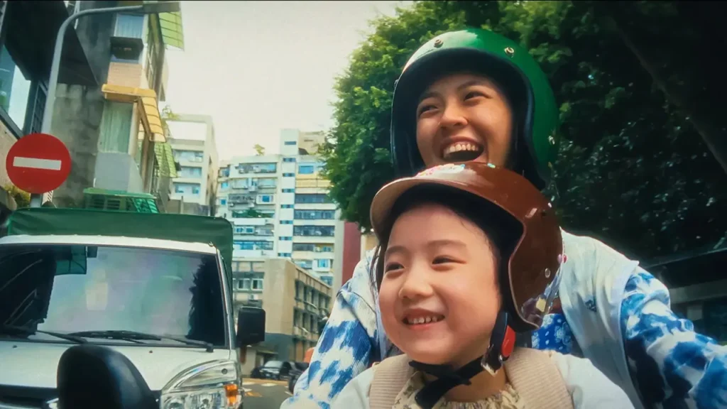 Mãe e filha sorrindo juntas enquanto andam de moto pelas ruas de Taipé no filme A Garota Canhota.
