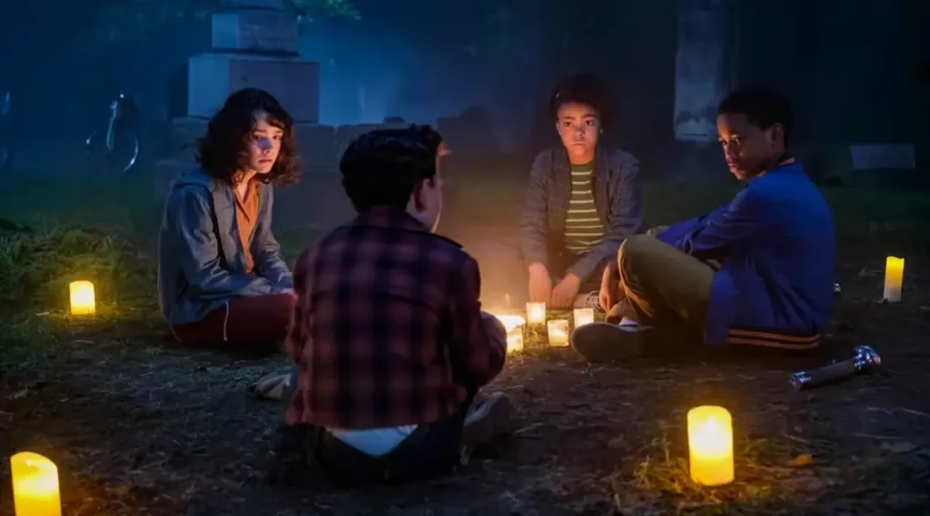 Crianças reunidas em um cemitério à noite, iluminadas por velas, em cena de It: Bem-Vindos a Derry