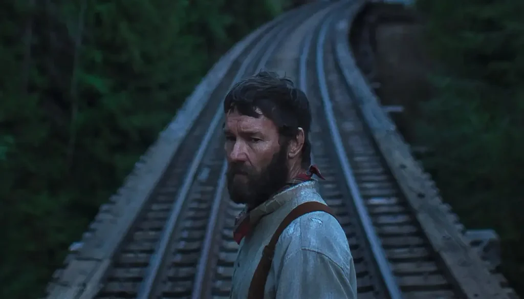 Robert olhando para trás enquanto caminha pelos trilhos no filme Sonhos de Trem