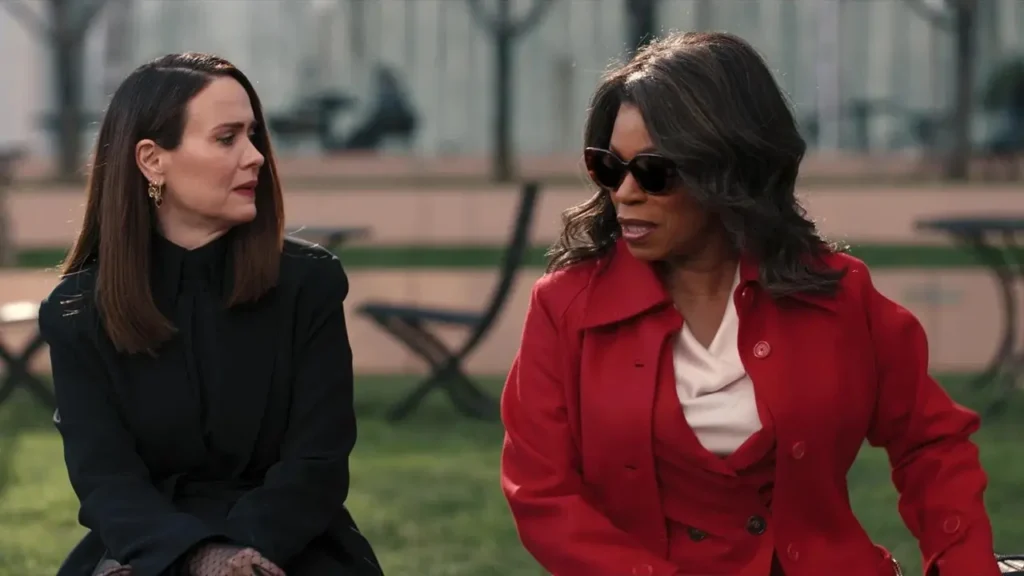 Personagens conversam em um banco ao ar livre em Tudo É Justo, com expressão séria durante uma cena dramática