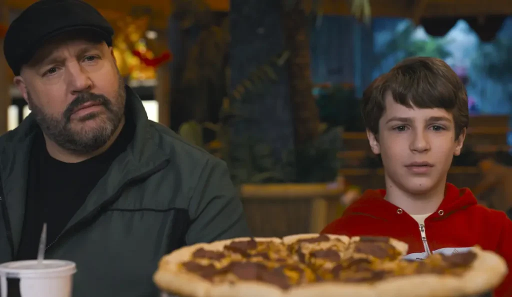 Brian e Lucas observam atentamente uma pizza durante uma sequência leve de Um Dia Fora de Controle