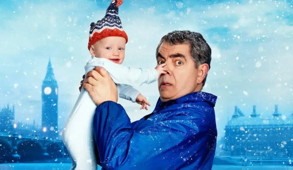 Rowan Atkinson segurando um bebê em cena da minissérie Homem X Bebê da Netflix