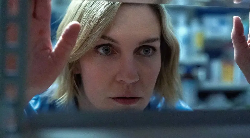 Carol Sturka observando atentamente uma prateleira enquanto busca pistas na série Pluribus, exibida na Apple TV+.