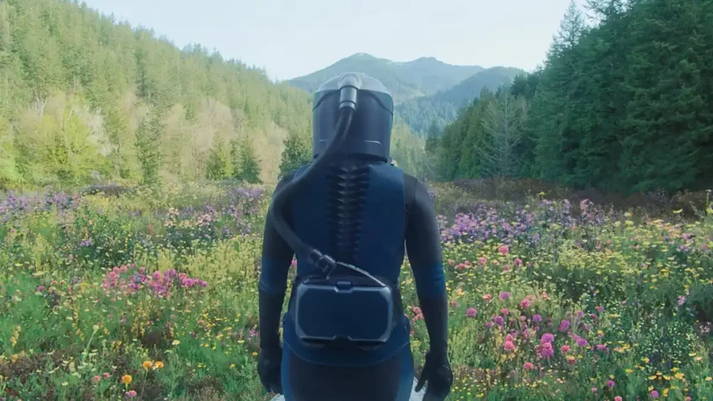 Cena de Em Um Piscar de Olhos mostra astronauta em traje espacial diante de campo florido cercado por montanhas