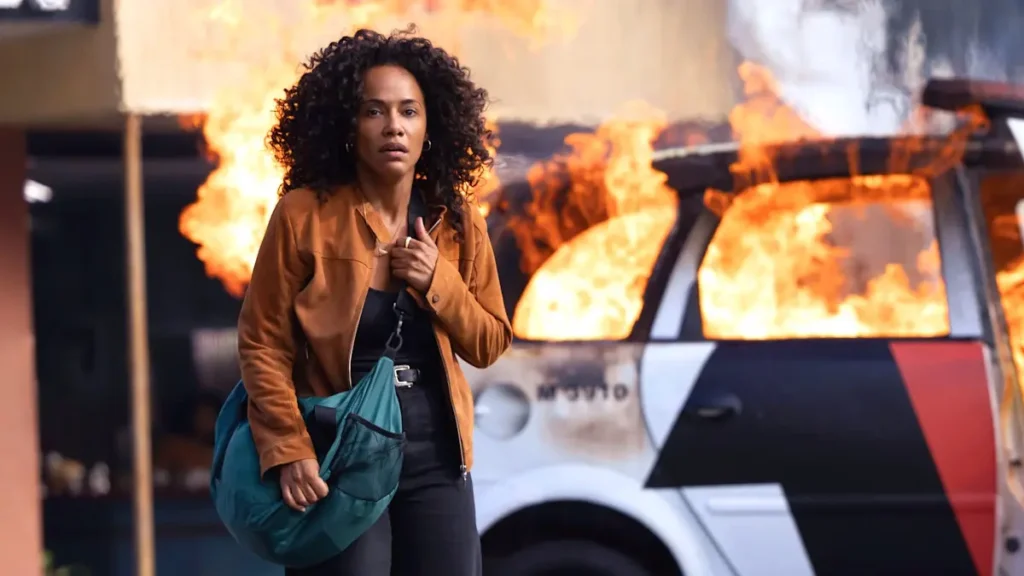 Cena de Salve Geral: Irmandade mostra personagem em meio a incêndio e viatura em chamas durante ataque urbano