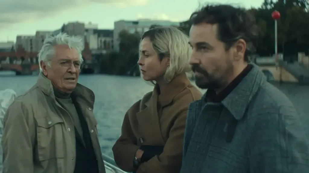 Simon e Meret conversam com um antigo contato ligado ao serviço de inteligência em cena tensa à beira de um rio em Unfamiliar