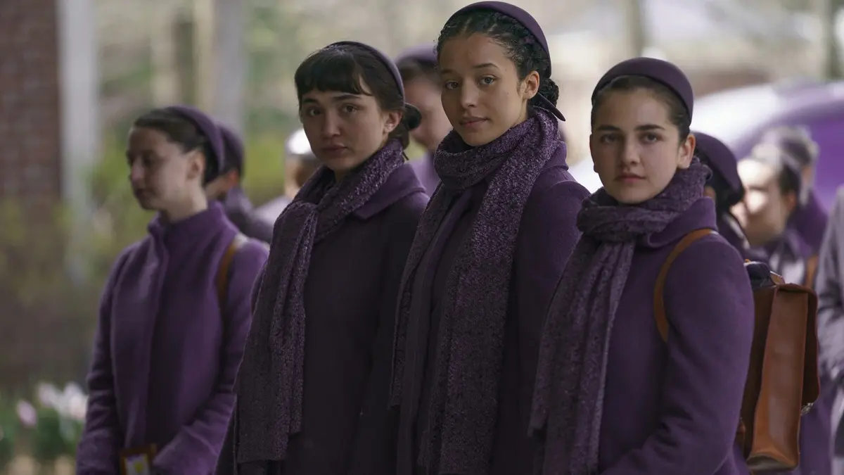Cena de Os Testamentos: Das Filhas de Gilead mostra Agnes ao lado de outras jovens vestidas de roxo em Gilead