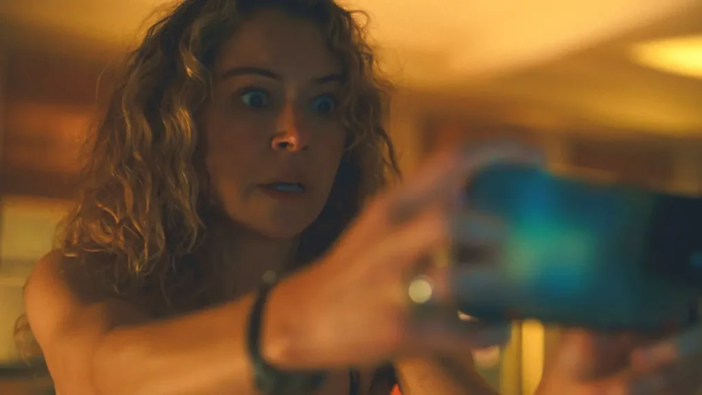 Tatiana Maslany aparece assustada em cena de Prazer Máximo Garantido enquanto segura um objeto em ambiente com iluminação quente