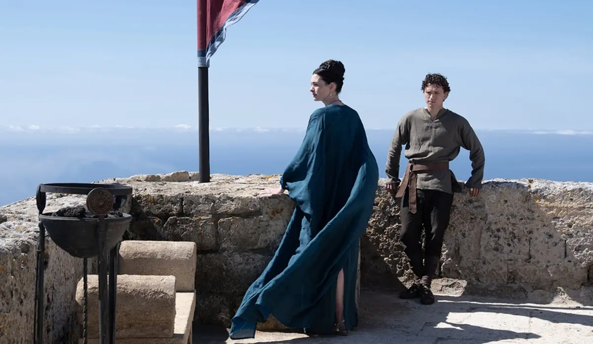 Tom Holland e Anne Hathaway aparecem caracterizados em cena de A Odisseia, em um cenário rochoso à beira-mar.