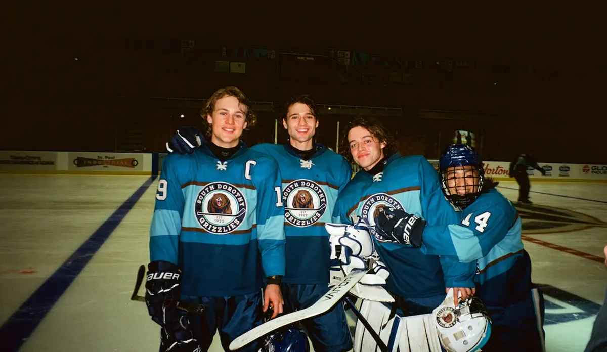 Jovens jogadores de The Sticks posam juntos em uma pista de hóquei usando uniformes do South Dorothy Grizzlies