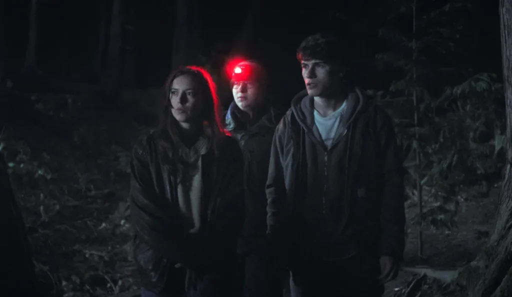 Amigos de Sonny investigam uma floresta durante a noite na série Fingida do Disney+
